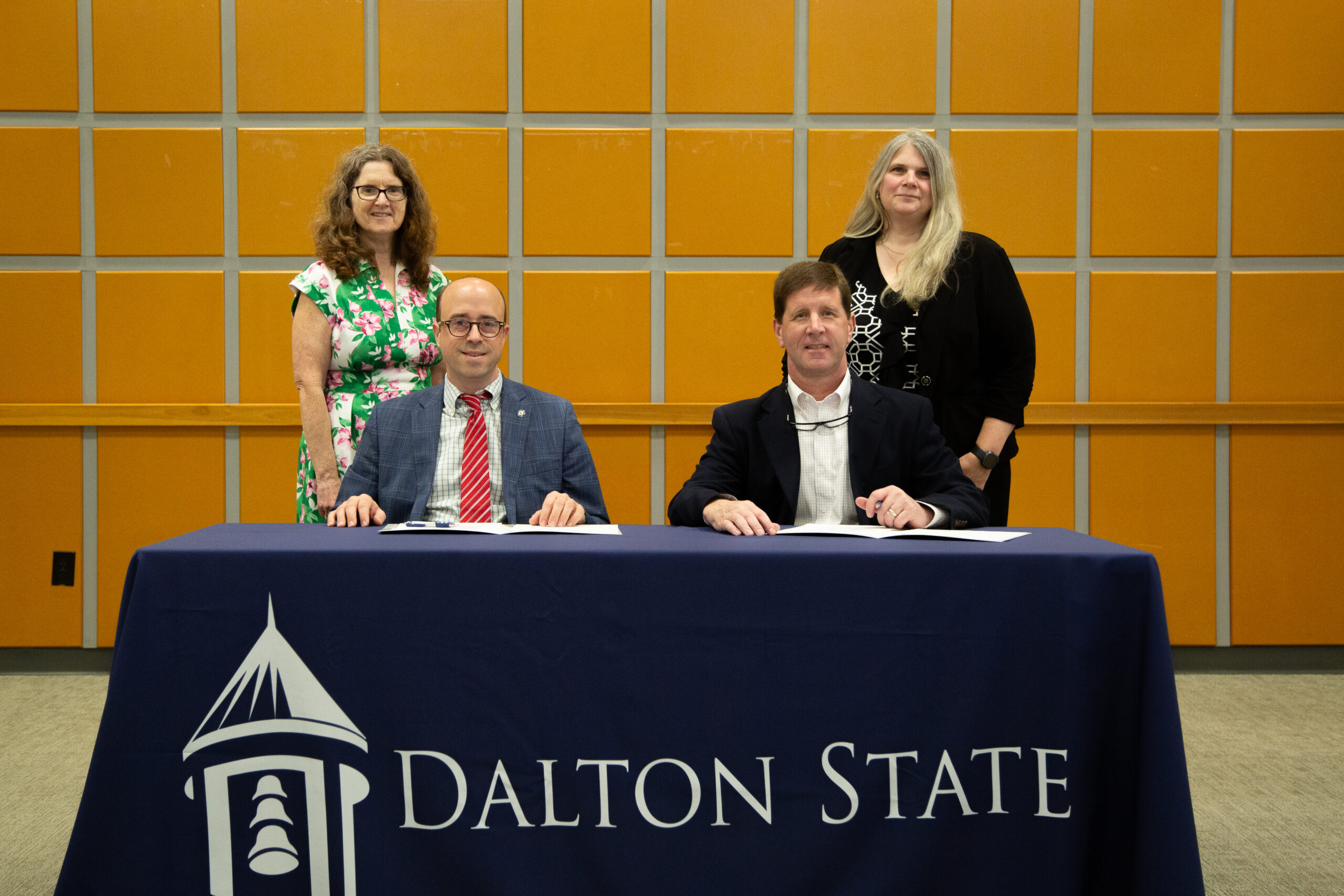 Dalton State President John Fuchko and Josh Ingle, superintendent of Dade County Schools, seated at a table. Sharon Hixon, dean of the School of Health Professions, and Gina Kertulis-Tartar, provost, are standing behind them.